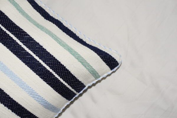 Détail de la housse de coussin tissée et cousue à la main avec des rayures bleu marine, bleu ciel et vert d'eau